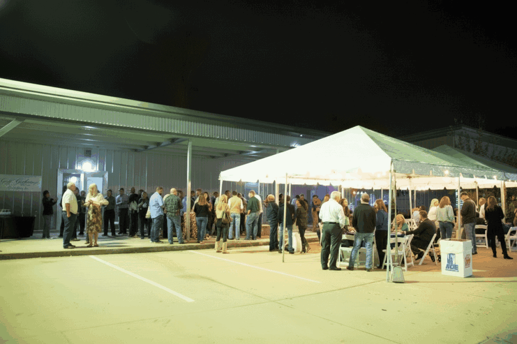 People gathering at a Gulf Coast outdoor event with a large tent, showcasing Gulf Coast hospitality, events, and community ambiance.