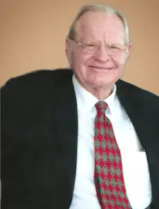 A professional elderly man smiling in a suit and tie, representing Gulf Coast gatherings, spotlighting community, networking, and event services.